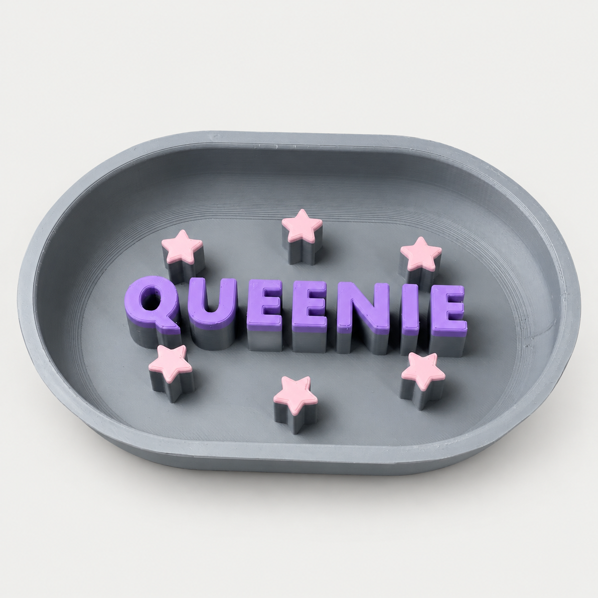 Grauer personalisierter Slowfeeder QUEENIE mit violetten Buchstaben und rosa Sternen auf neutralgrauem Hintergrund